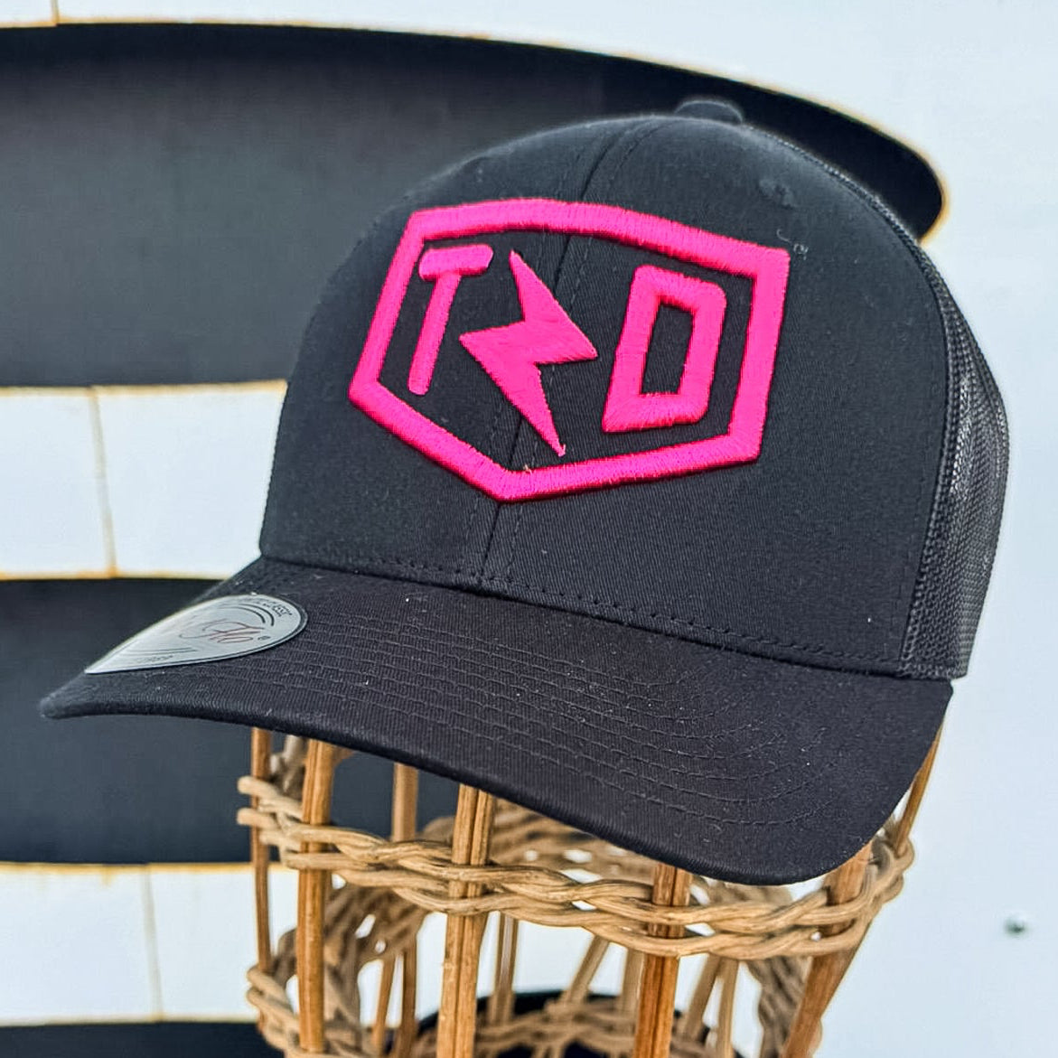 Black cap with pink logo on a mannequin head against a striped background